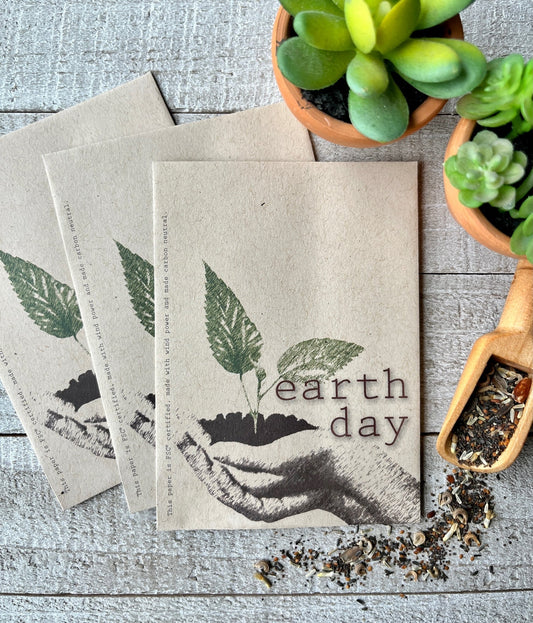 Three brown seed packets with a picture of hands holding soil and a green sprout.