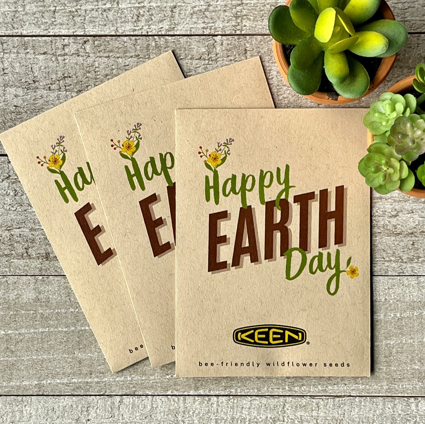 Three brown seed packets that say "Happy Earth Day," with flowers blooming from the H and Y.